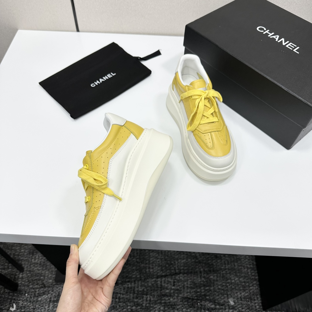A pair of luxury Chanel yellow and white platform sneakers displayed on a black box with a branded dust bag. - Hình 9