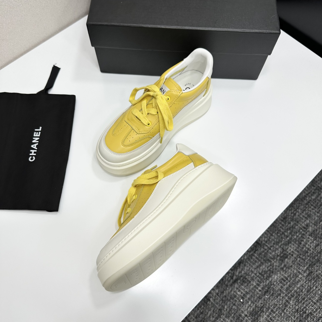 A pair of luxury Chanel yellow and white platform sneakers displayed on a black box with a branded dust bag. - Hình 5