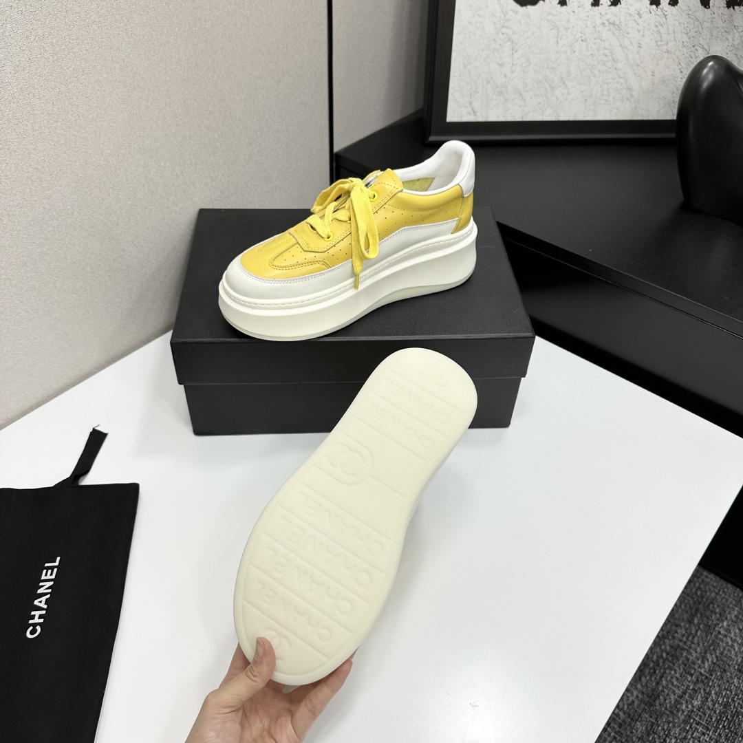 A pair of luxury Chanel yellow and white platform sneakers displayed on a black box with a branded dust bag. - Hình 4