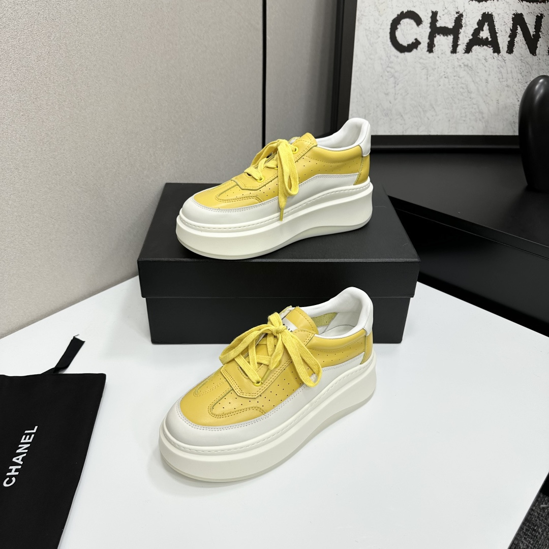 A pair of luxury Chanel yellow and white platform sneakers displayed on a black box with a branded dust bag. - Hình 2