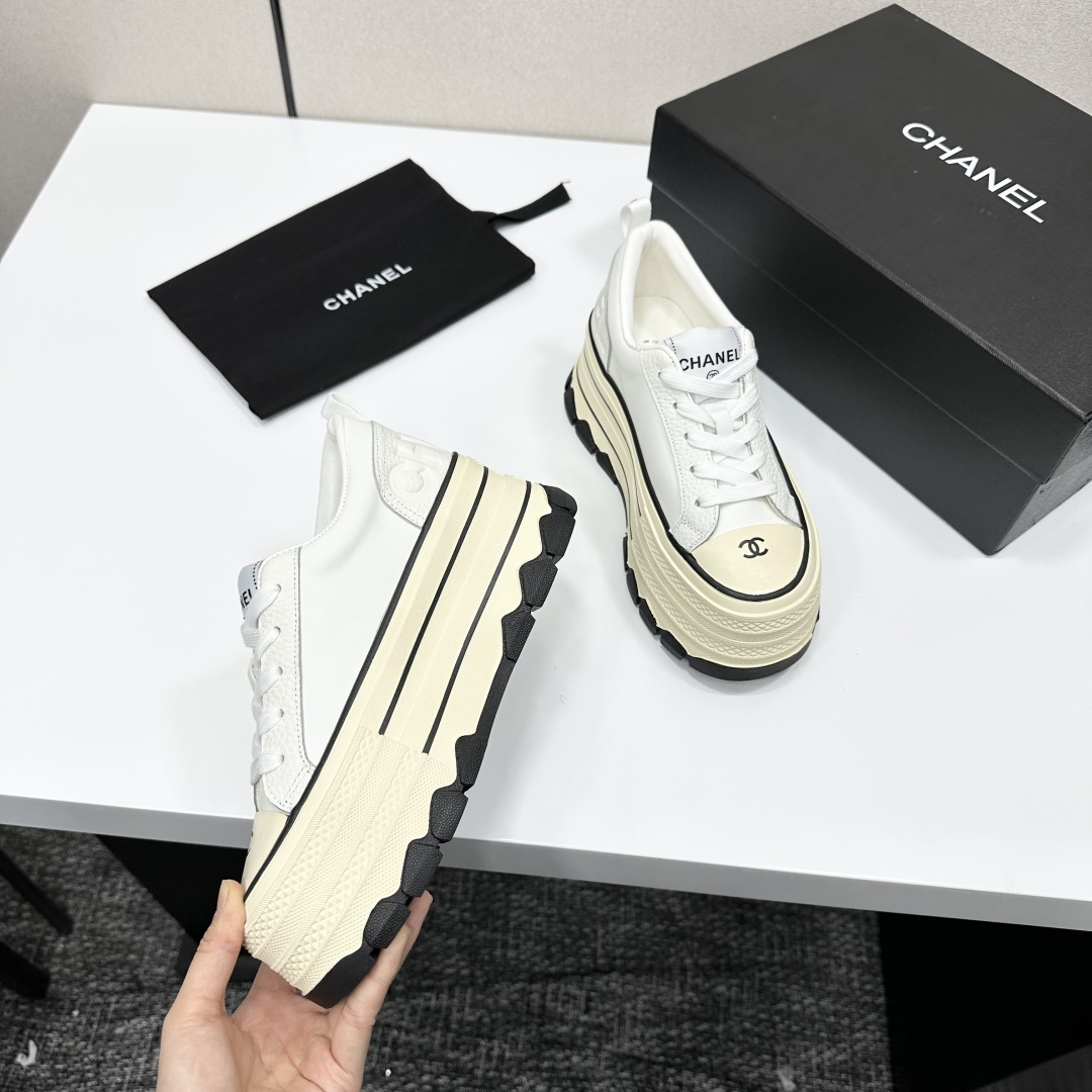 A pair of Chanel white leather platform sneakers with a thick cream sole and black accents, displayed on a black box. - Hình 9