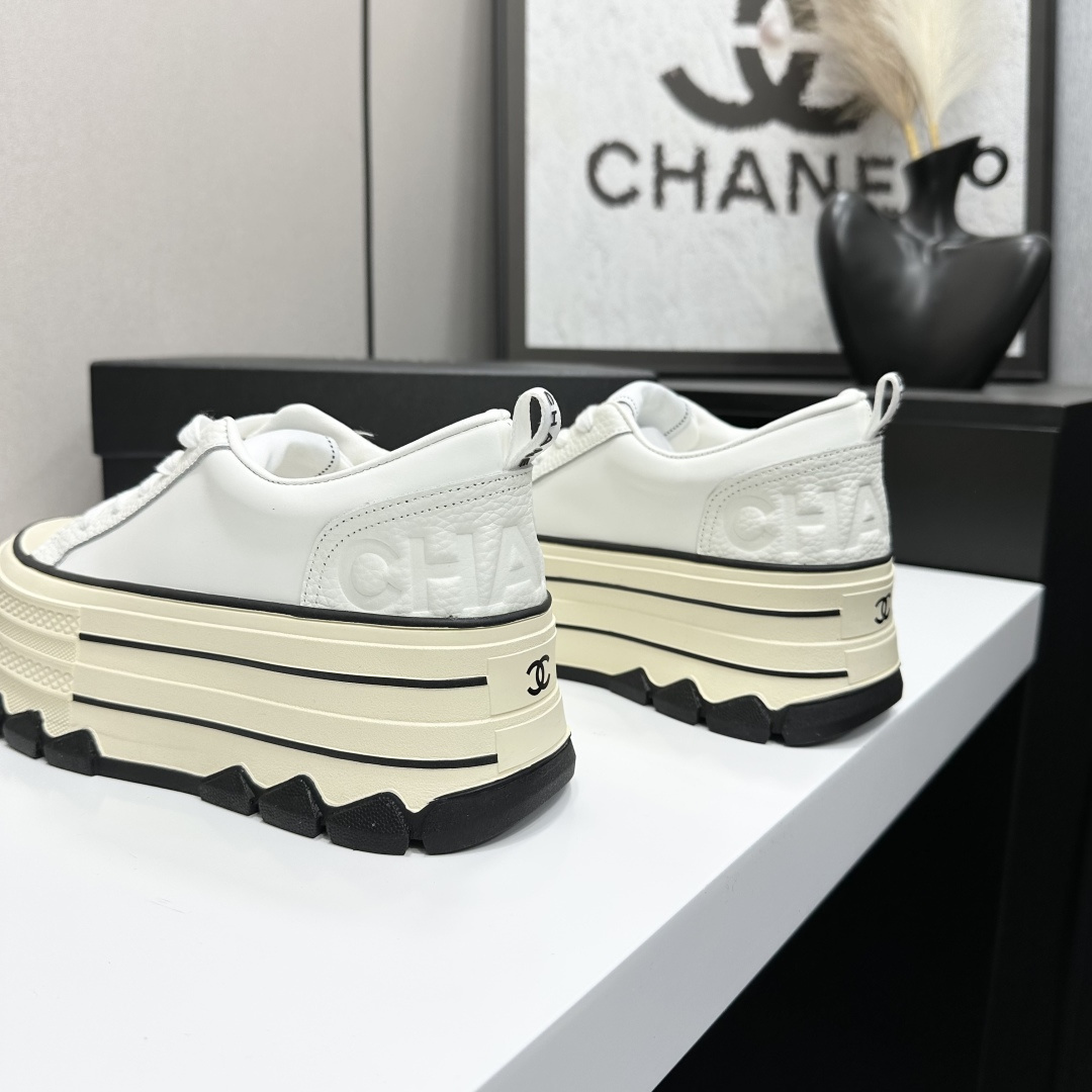 A pair of Chanel white leather platform sneakers with a thick cream sole and black accents, displayed on a black box. - Hình 6