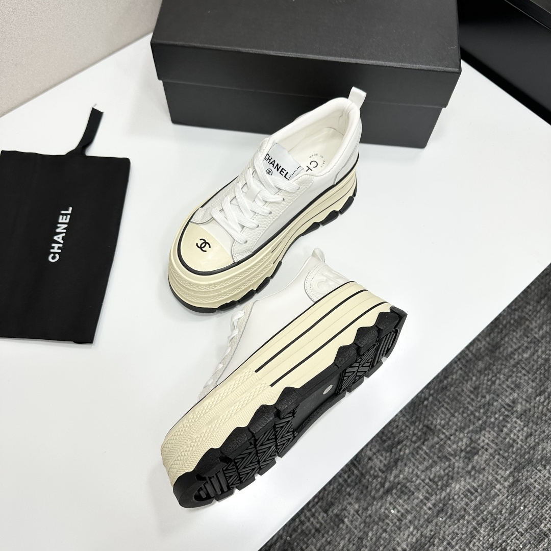 A pair of Chanel white leather platform sneakers with a thick cream sole and black accents, displayed on a black box. - Hình 5