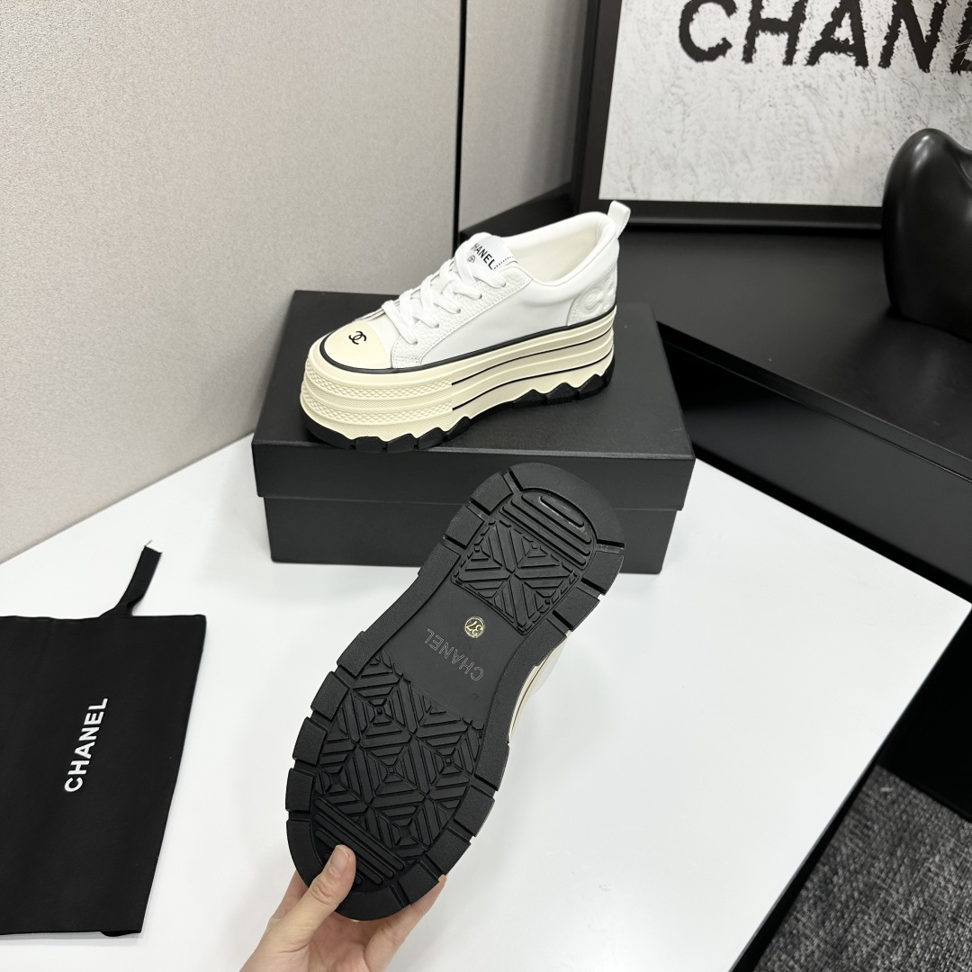 A pair of Chanel white leather platform sneakers with a thick cream sole and black accents, displayed on a black box. - Hình 4