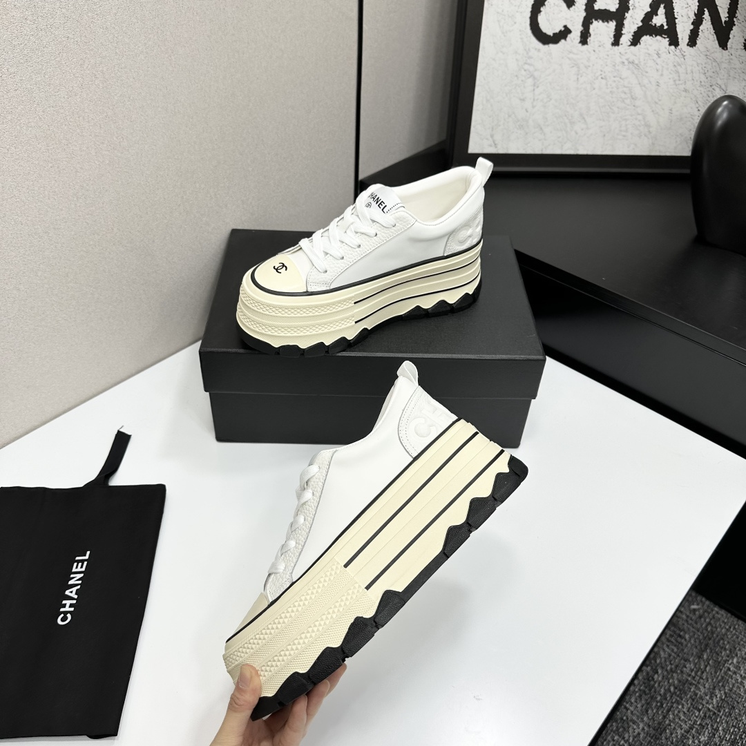 A pair of Chanel white leather platform sneakers with a thick cream sole and black accents, displayed on a black box. - Hình 3