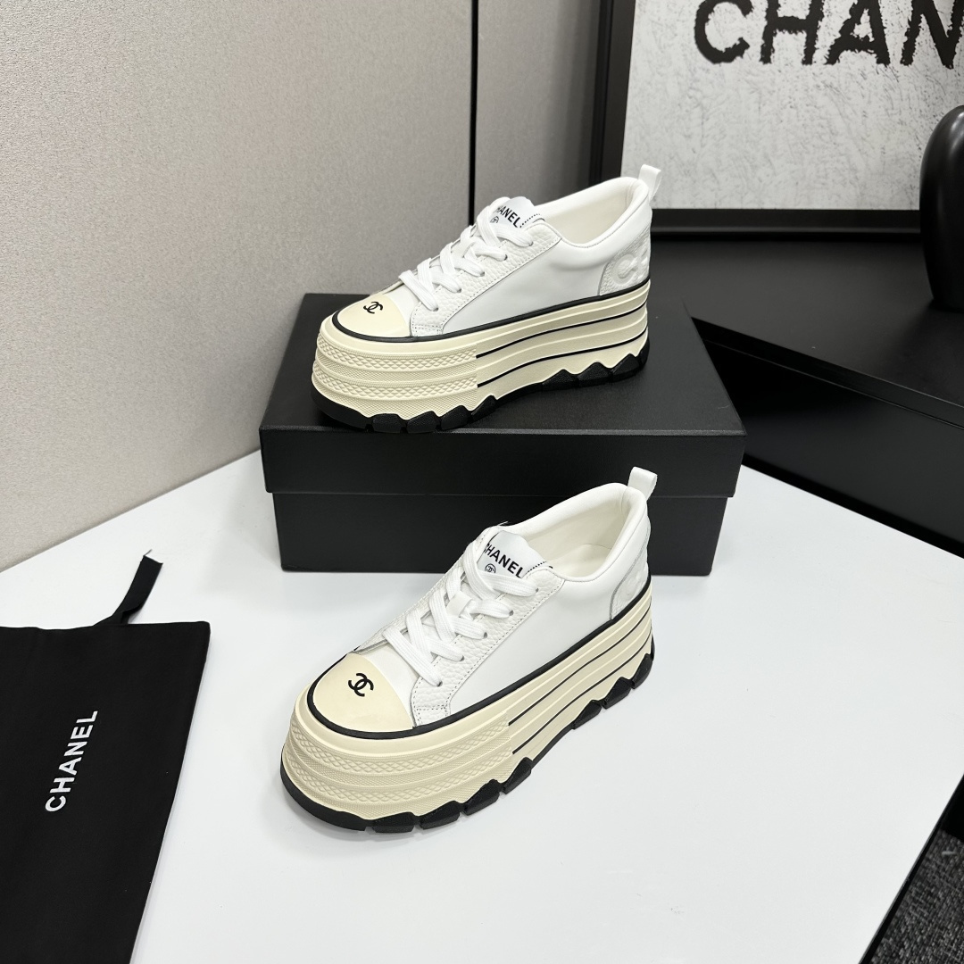 A pair of Chanel white leather platform sneakers with a thick cream sole and black accents, displayed on a black box. - Hình 2