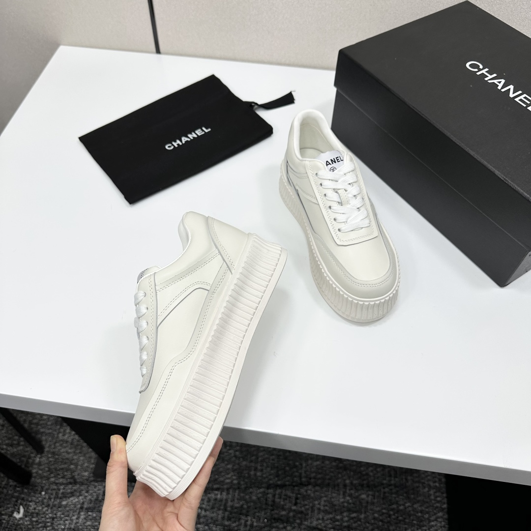 A pair of Chanel white leather platform sneakers with interlocking CC logo displayed on a black designer box. - Hình 2