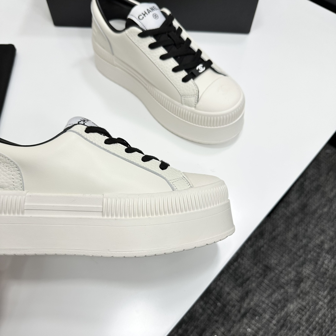 A pair of luxury Chanel white leather platform sneakers with black laces displayed on a black box. - Hình 8