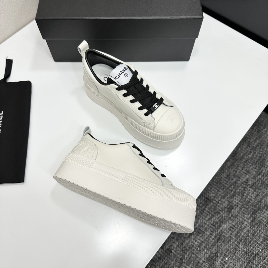 A pair of luxury Chanel white leather platform sneakers with black laces displayed on a black box. - Hình 7
