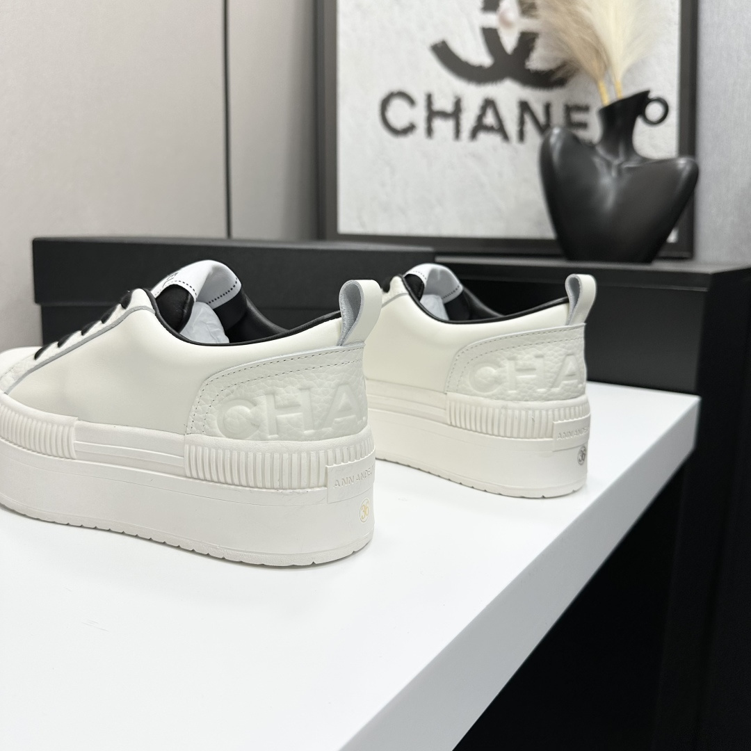 A pair of luxury Chanel white leather platform sneakers with black laces displayed on a black box. - Hình 6