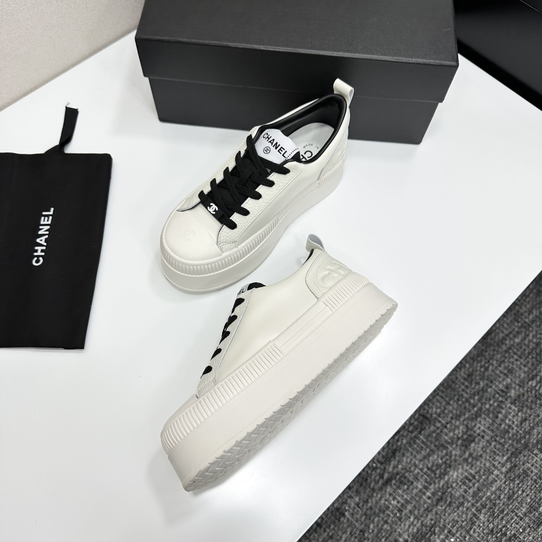 A pair of luxury Chanel white leather platform sneakers with black laces displayed on a black box. - Hình 5