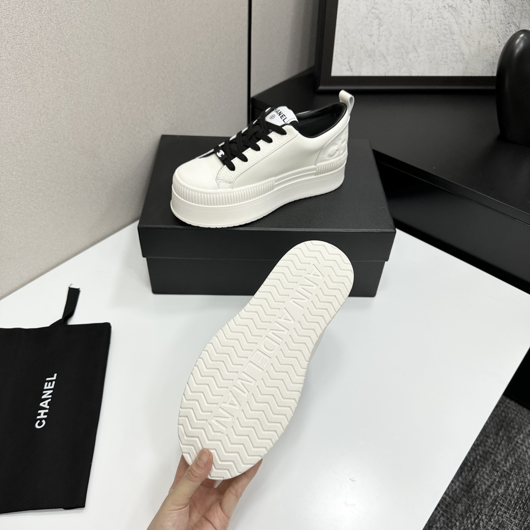A pair of luxury Chanel white leather platform sneakers with black laces displayed on a black box. - Hình 4