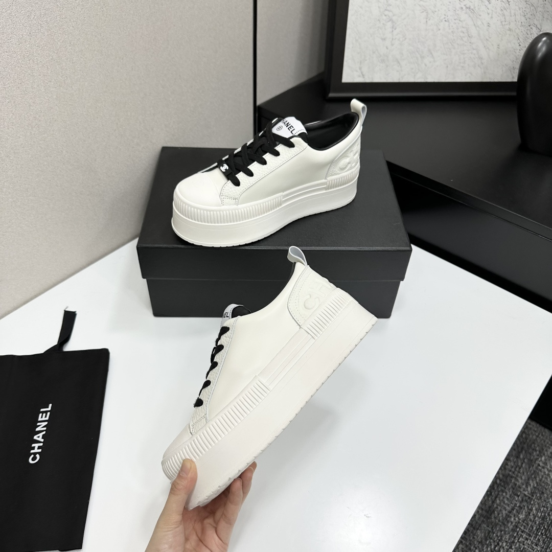 A pair of luxury Chanel white leather platform sneakers with black laces displayed on a black box. - Hình 3