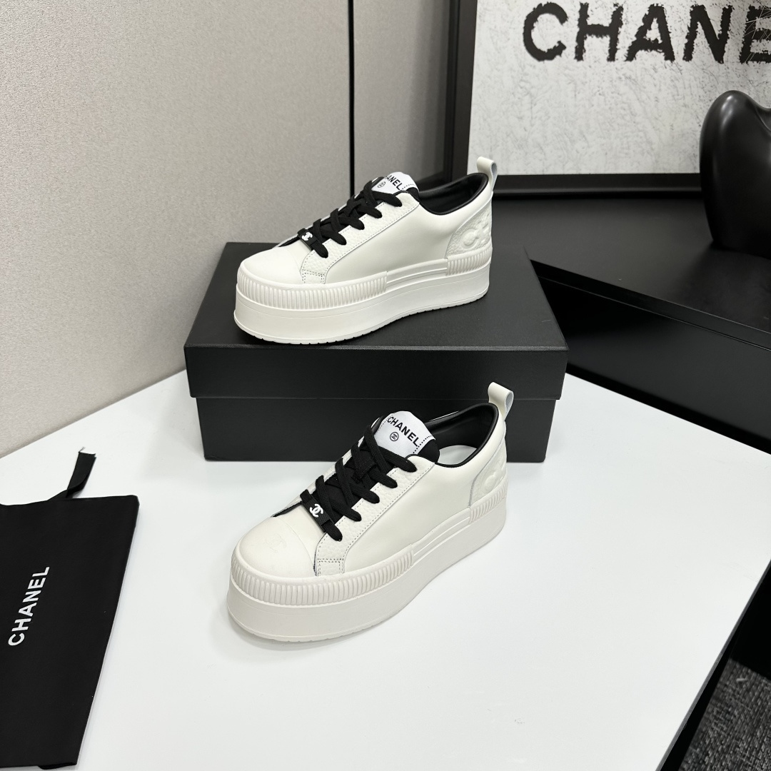 A pair of luxury Chanel white leather platform sneakers with black laces displayed on a black box. - Hình 2