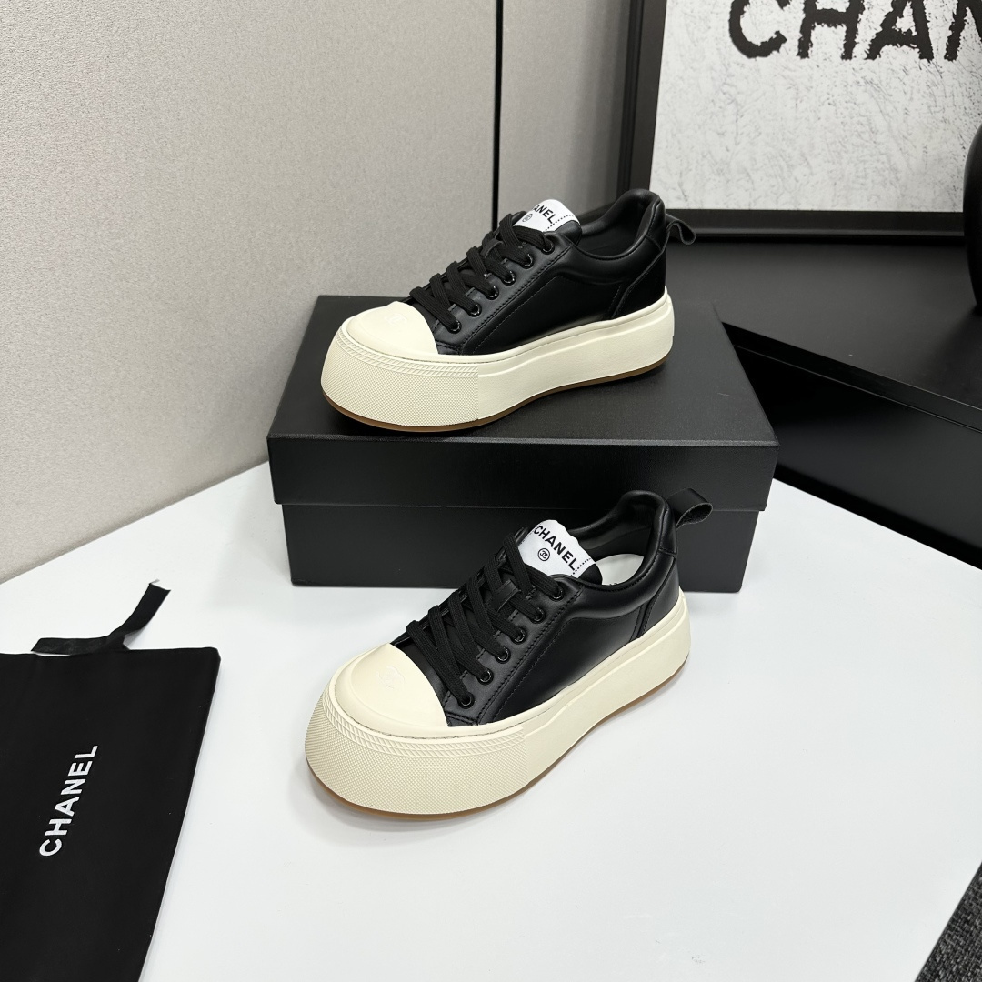 A pair of Chanel black leather sneakers with a thick cream platform sole placed on a black designer box. - Hình 2