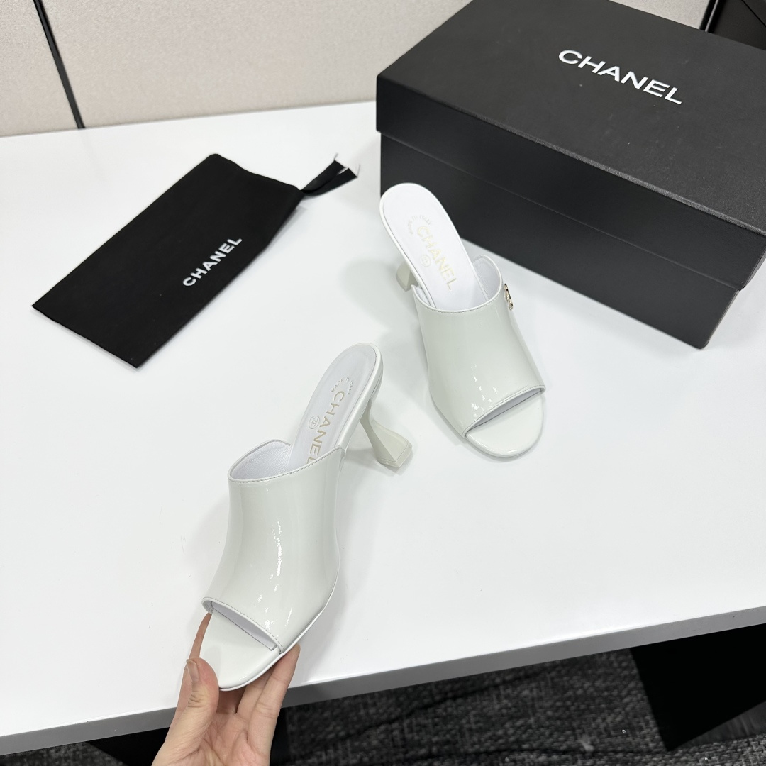 A pair of Chanel white patent leather open-toe mules with gold CC logo and flared heels on a black box. - Hình 9