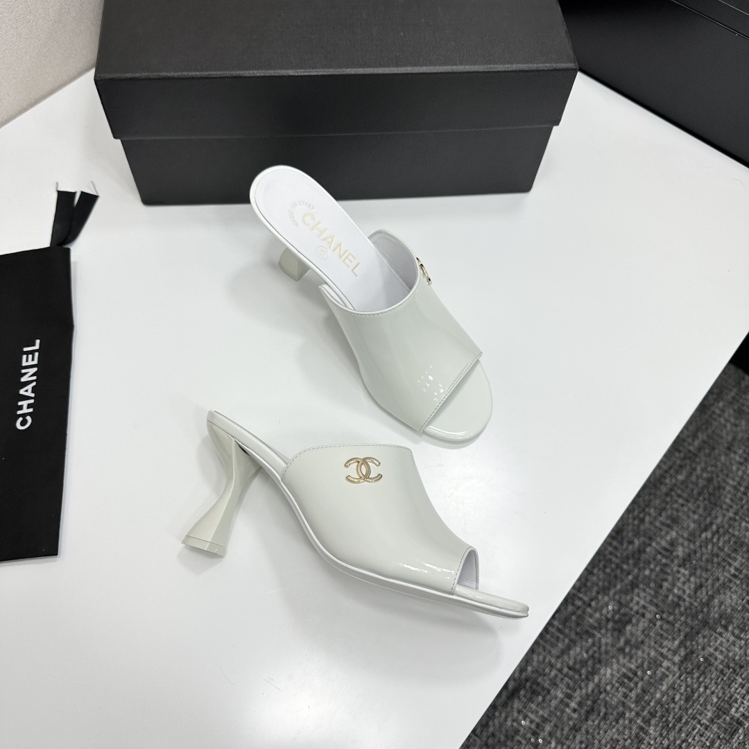 A pair of Chanel white patent leather open-toe mules with gold CC logo and flared heels on a black box. - Hình 8