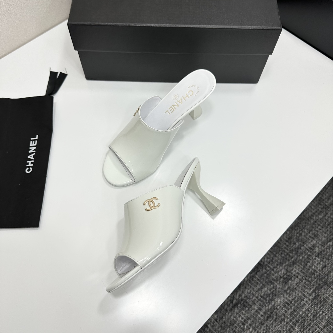 A pair of Chanel white patent leather open-toe mules with gold CC logo and flared heels on a black box. - Hình 6