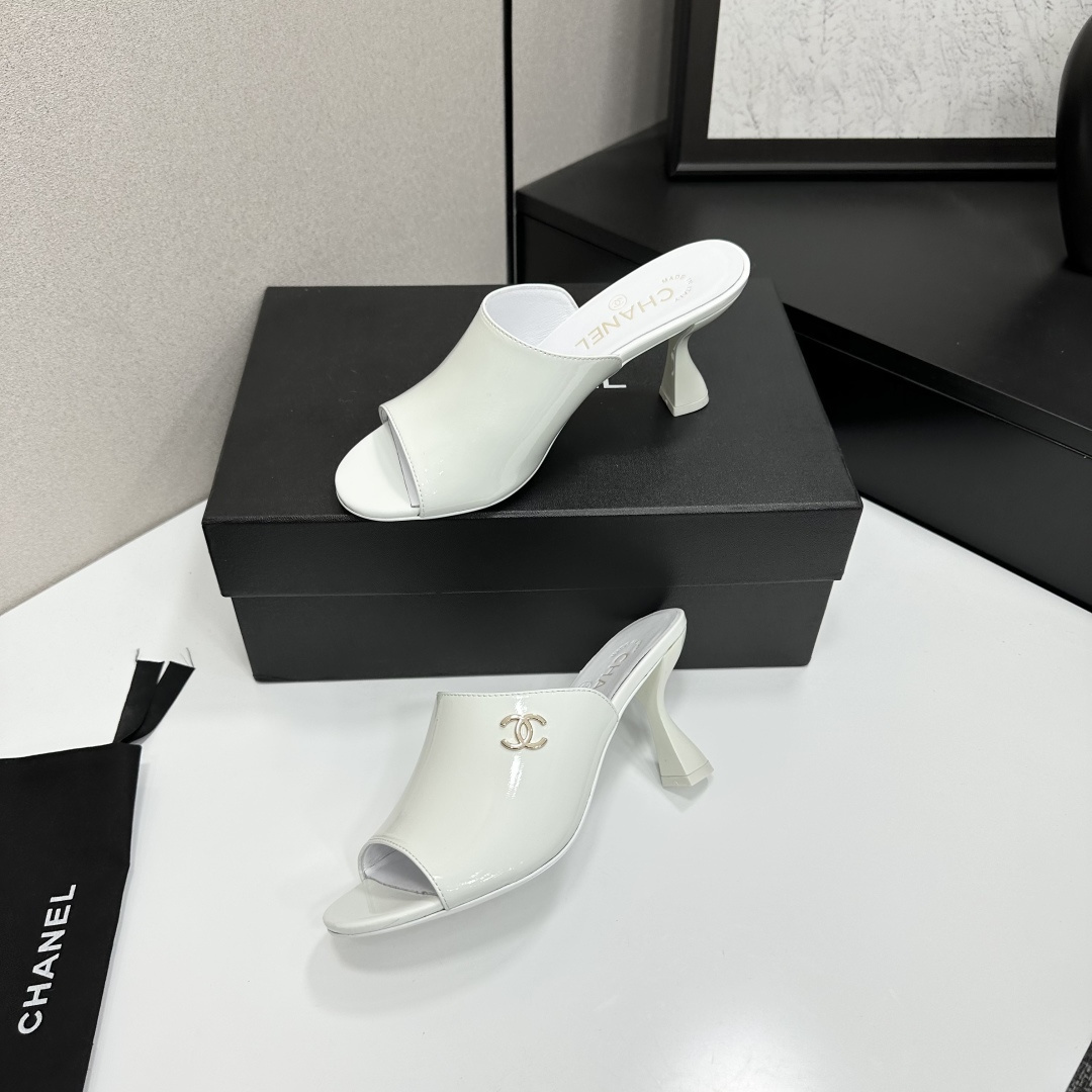 A pair of Chanel white patent leather open-toe mules with gold CC logo and flared heels on a black box. - Hình 3