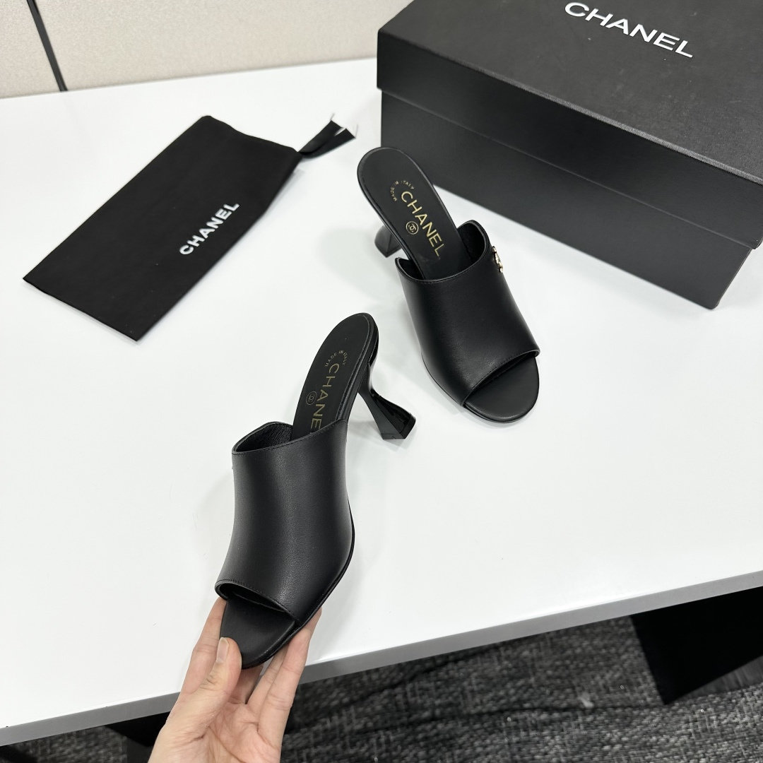 A pair of luxury Chanel black leather mule sandals with gold CC logos resting on a branded black box. - Hình 9