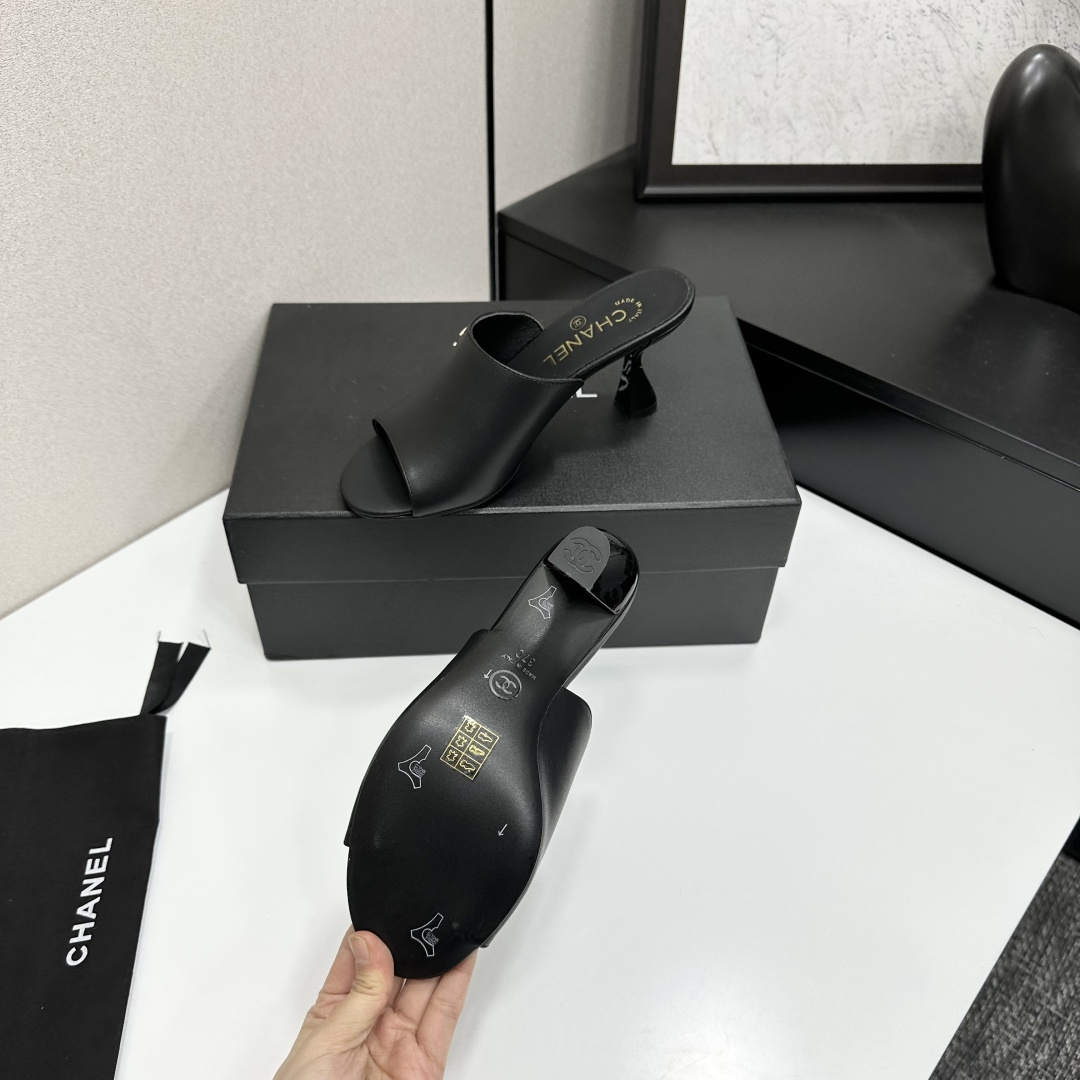 A pair of luxury Chanel black leather mule sandals with gold CC logos resting on a branded black box. - Hình 5