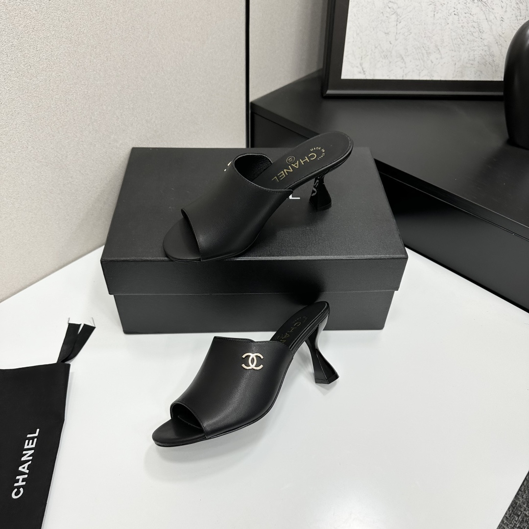 A pair of luxury Chanel black leather mule sandals with gold CC logos resting on a branded black box. - Hình 4