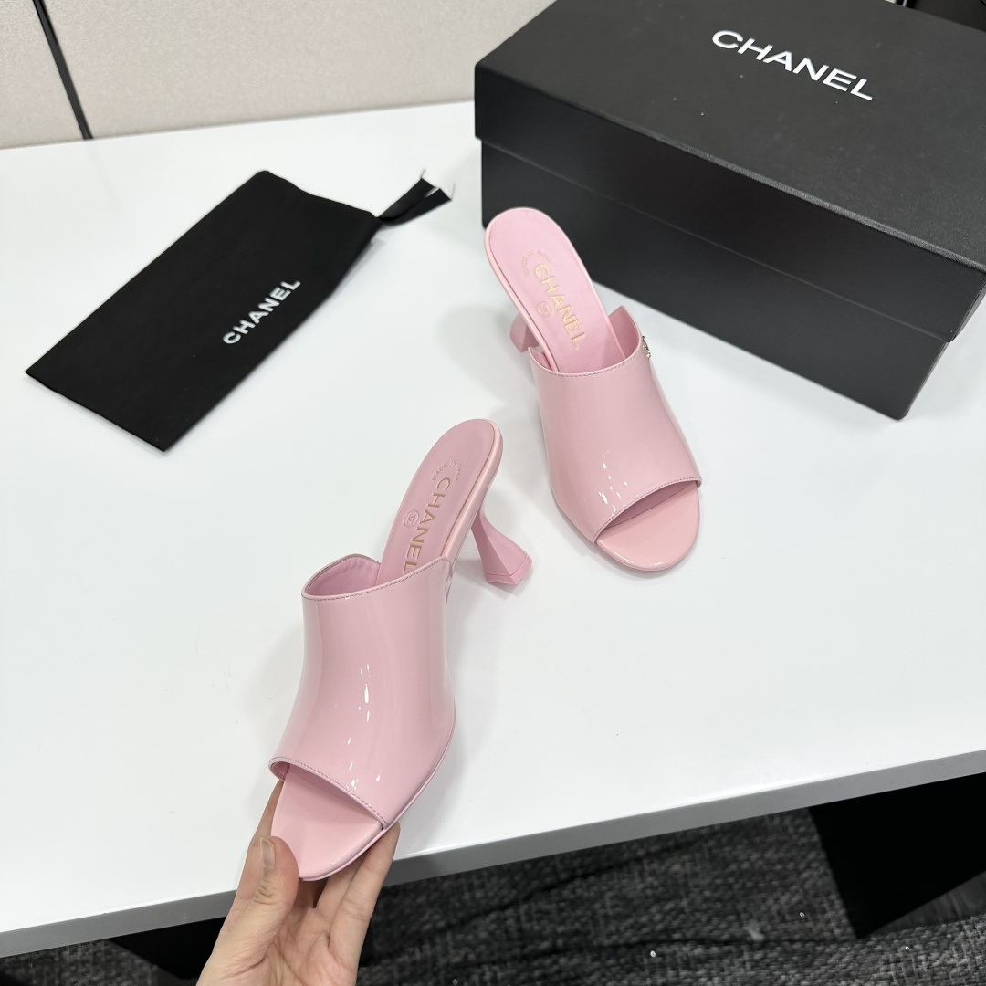 A pair of pink Chanel patent leather mules with gold CC logo and sculpted heels displayed on a black designer box. - Hình 9