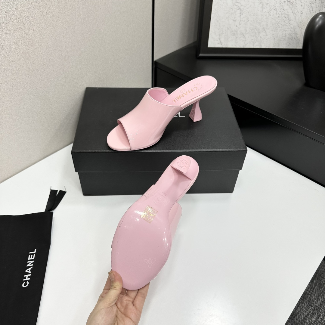 A pair of pink Chanel patent leather mules with gold CC logo and sculpted heels displayed on a black designer box. - Hình 4