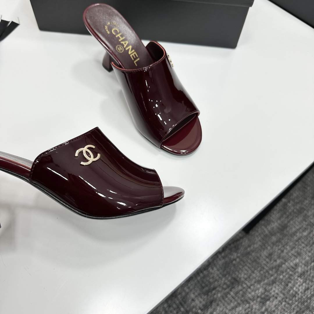 A pair of luxury Chanel burgundy patent leather open-toe mules with gold CC logo displayed on a black Chanel shoe box. - Hình 9