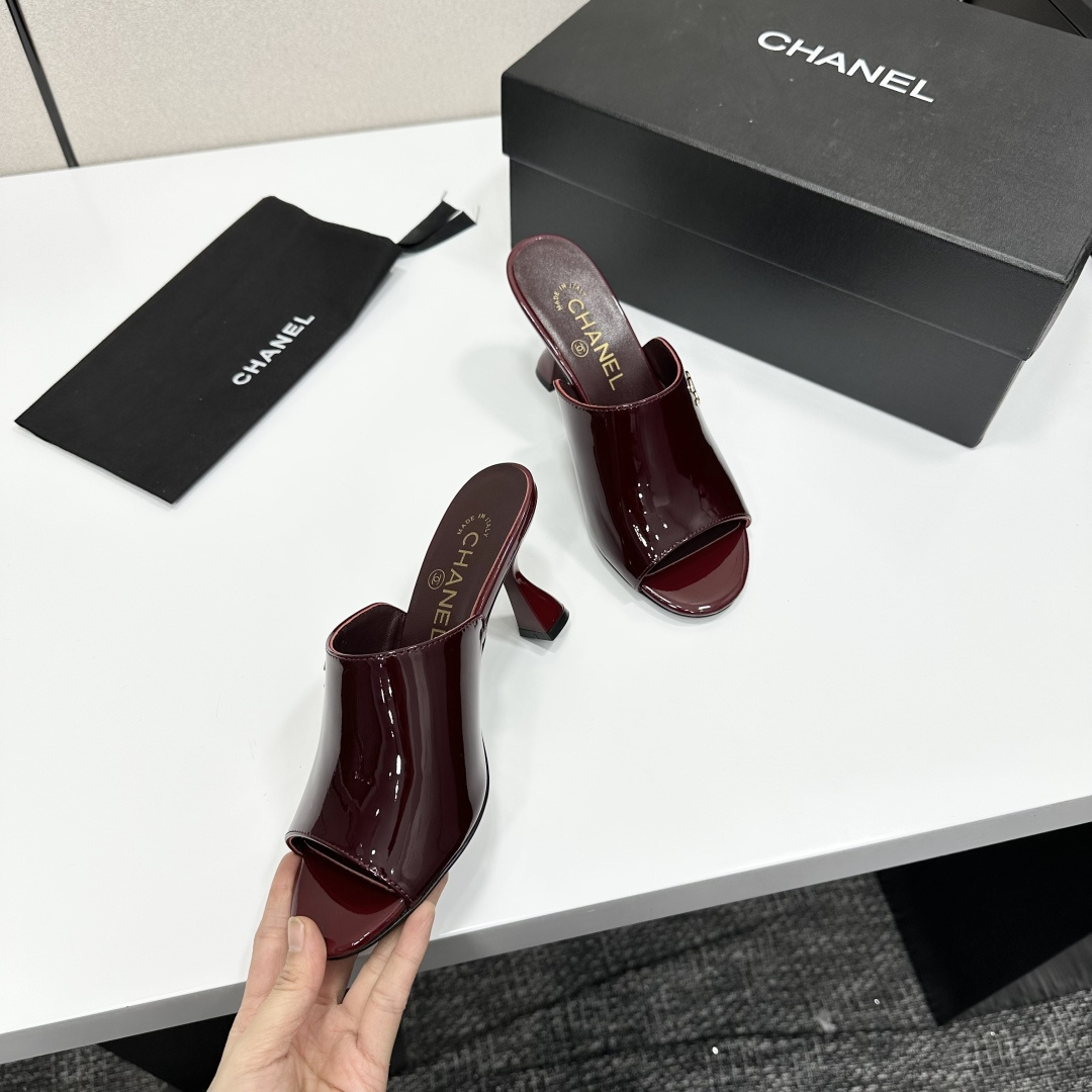 A pair of luxury Chanel burgundy patent leather open-toe mules with gold CC logo displayed on a black Chanel shoe box. - Hình 8