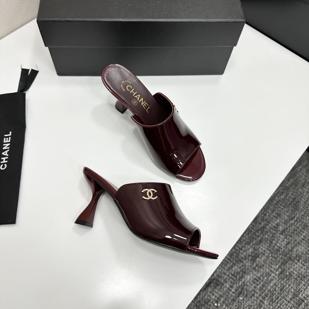 A pair of luxury Chanel burgundy patent leather open-toe mules with gold CC logo displayed on a black Chanel shoe box. - Hình 7