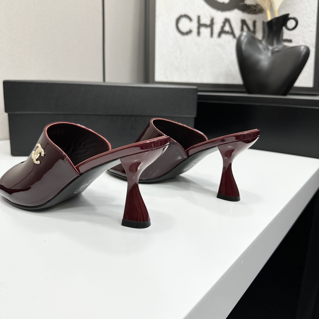 A pair of luxury Chanel burgundy patent leather open-toe mules with gold CC logo displayed on a black Chanel shoe box. - Hình 6