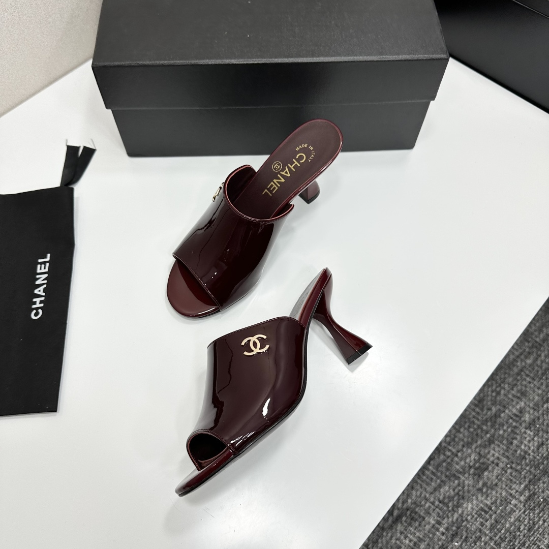 A pair of luxury Chanel burgundy patent leather open-toe mules with gold CC logo displayed on a black Chanel shoe box. - Hình 5