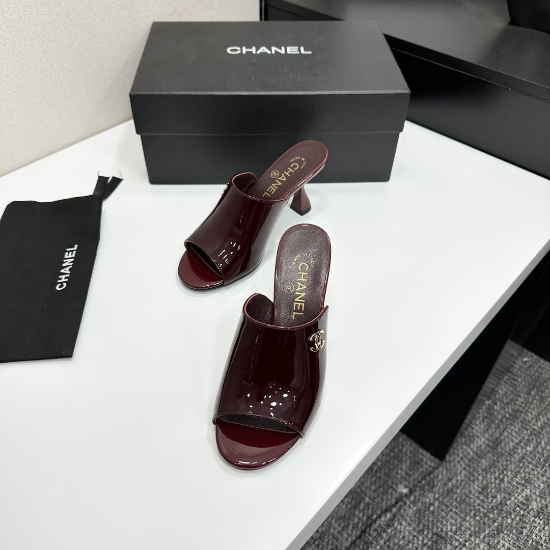 A pair of luxury Chanel burgundy patent leather open-toe mules with gold CC logo displayed on a black Chanel shoe box. - Hình 4