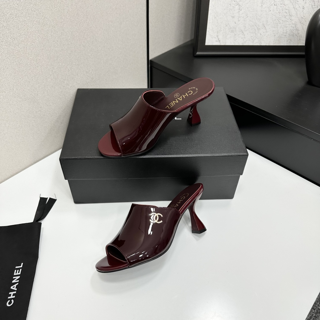 A pair of luxury Chanel burgundy patent leather open-toe mules with gold CC logo displayed on a black Chanel shoe box. - Hình 3