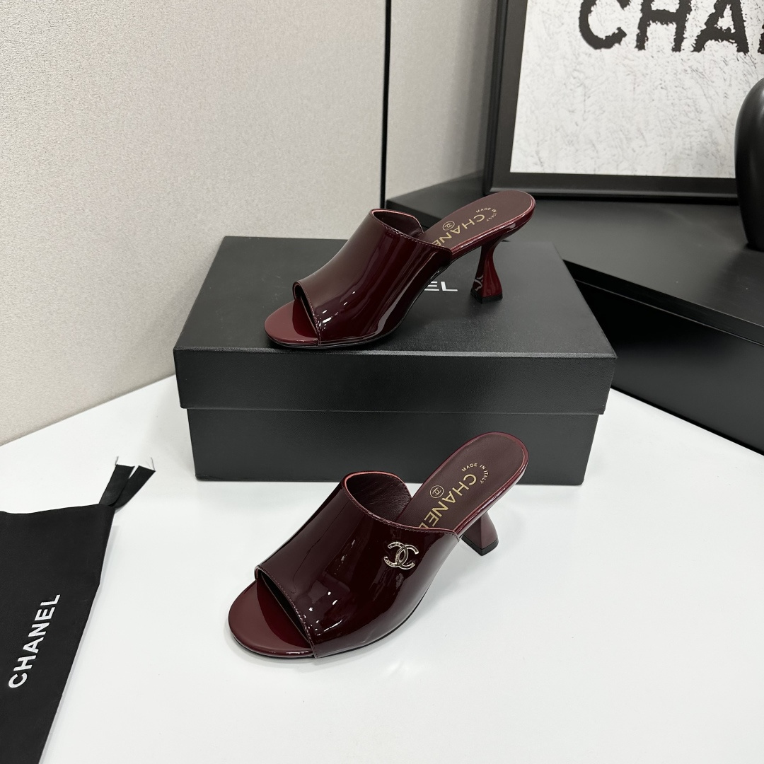 A pair of luxury Chanel burgundy patent leather open-toe mules with gold CC logo displayed on a black Chanel shoe box. - Hình 2