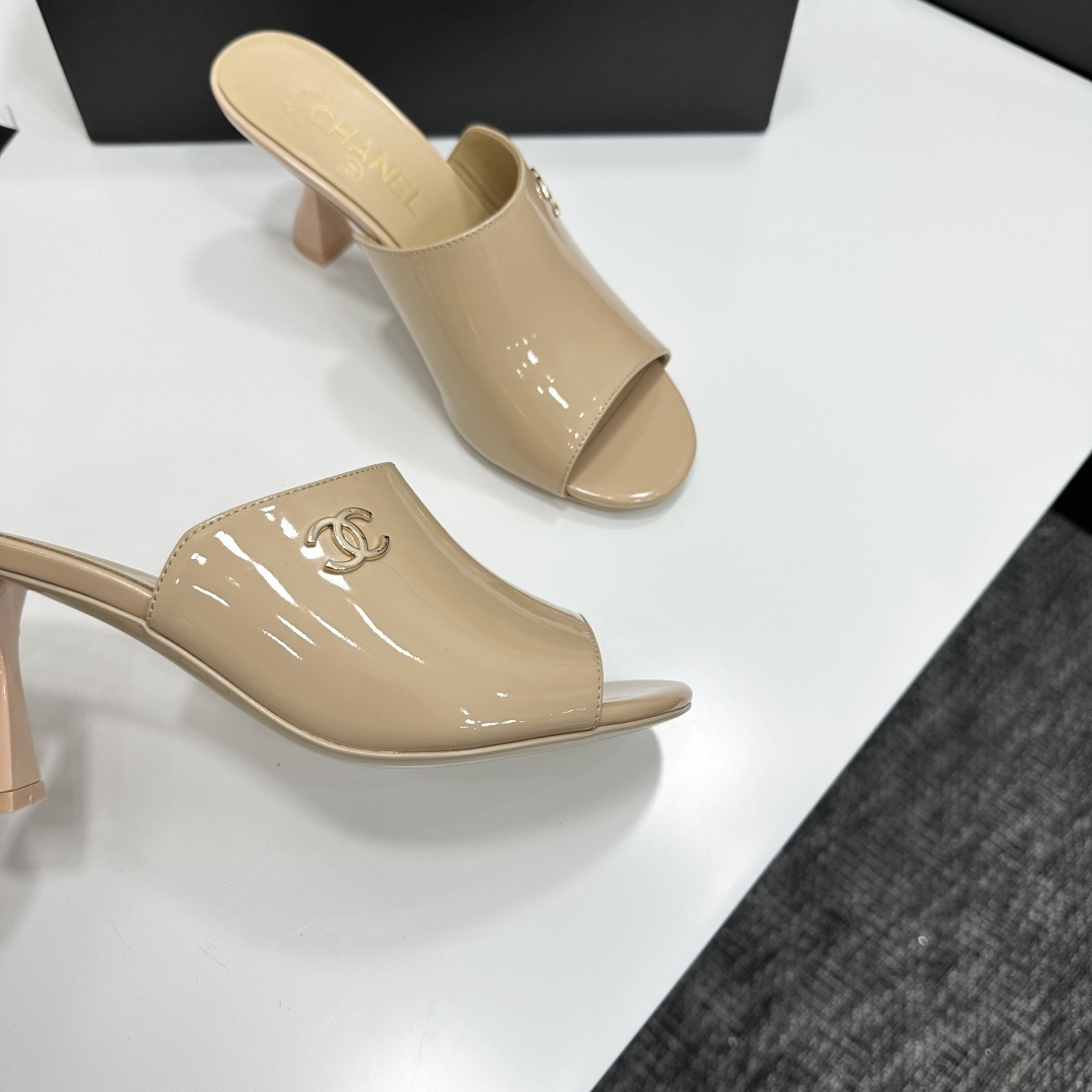 A pair of Chanel beige patent leather open-toe mules with gold CC logo and sculptural hourglass heels displayed on a black Chanel box. - Hình 10