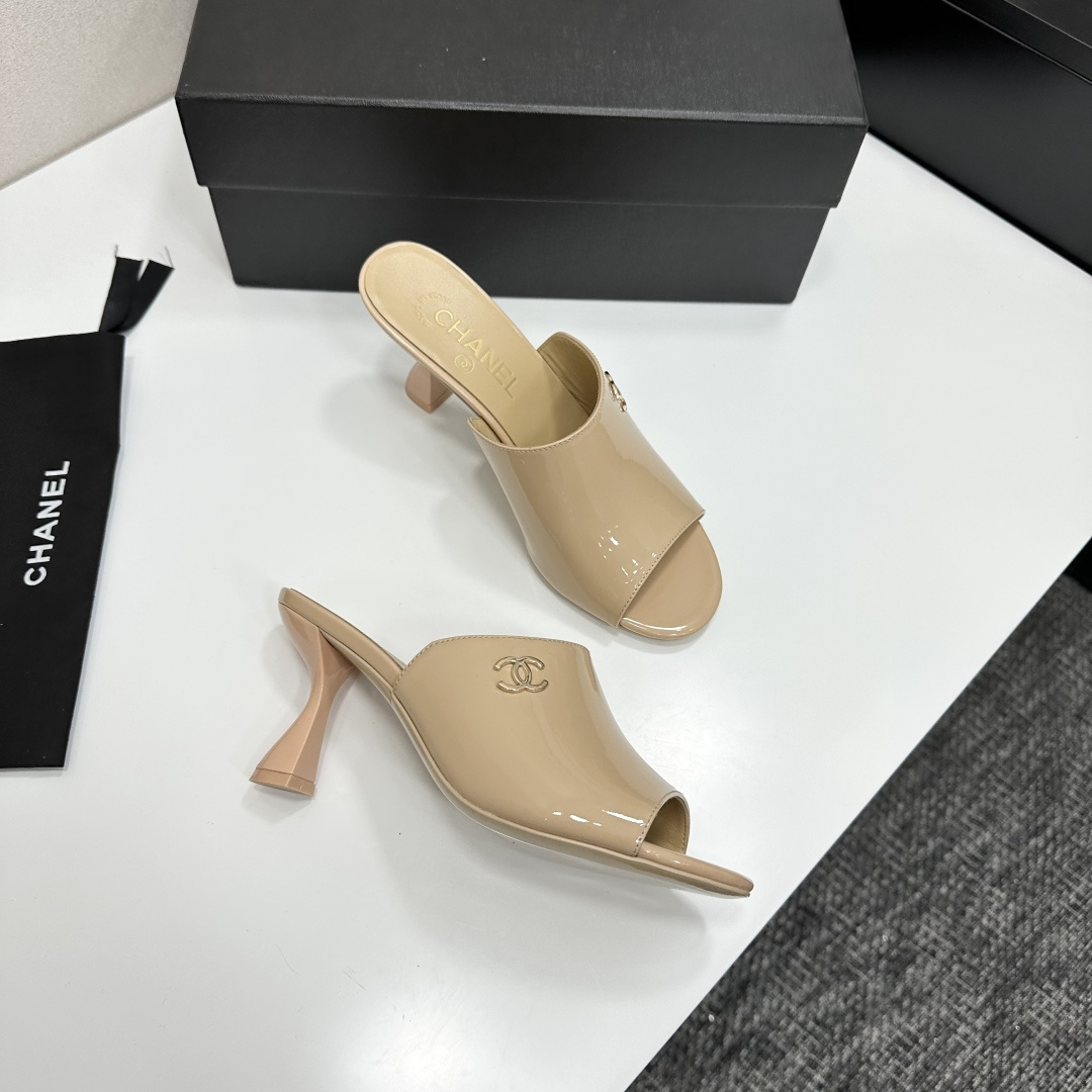 A pair of Chanel beige patent leather open-toe mules with gold CC logo and sculptural hourglass heels displayed on a black Chanel box. - Hình 9