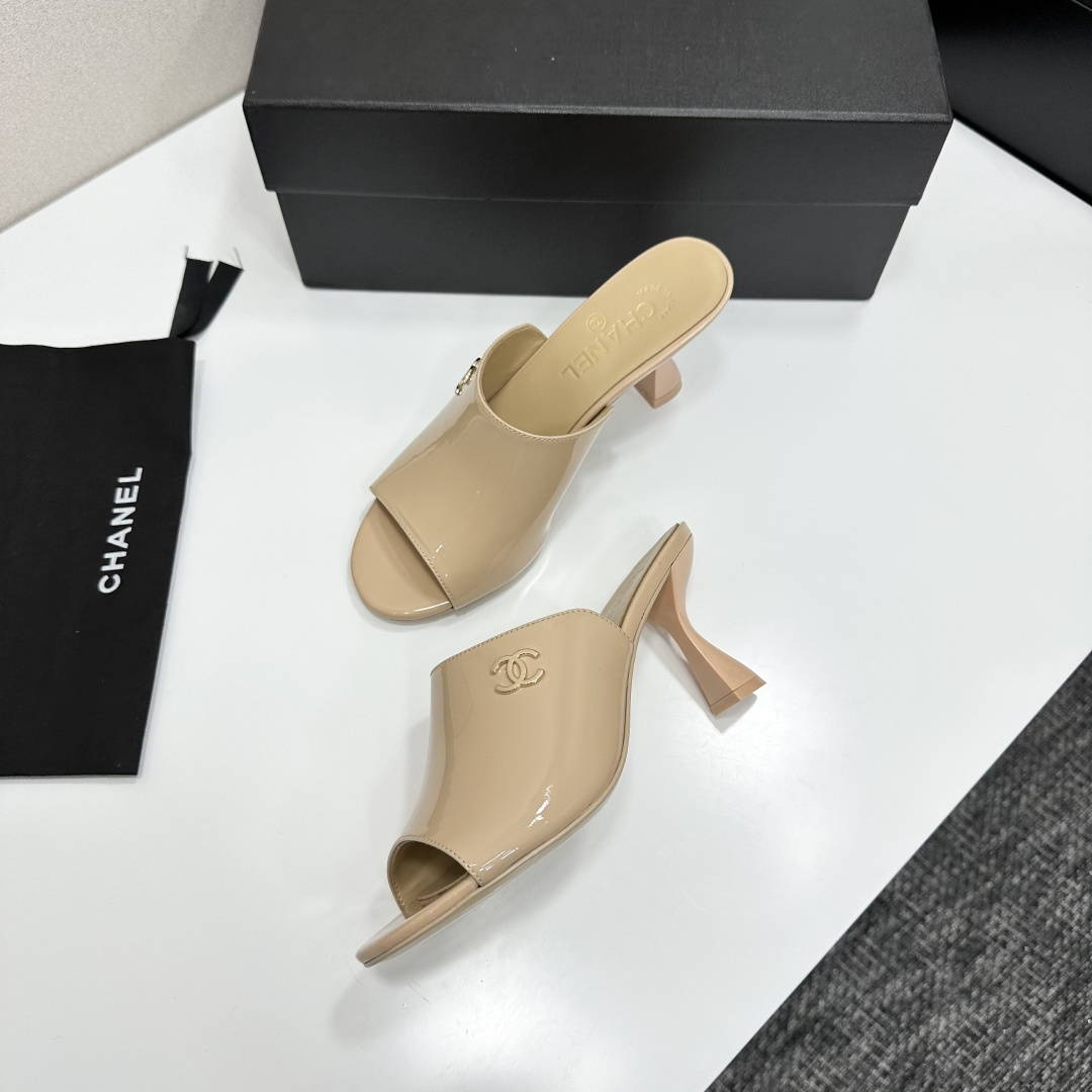 A pair of Chanel beige patent leather open-toe mules with gold CC logo and sculptural hourglass heels displayed on a black Chanel box. - Hình 7