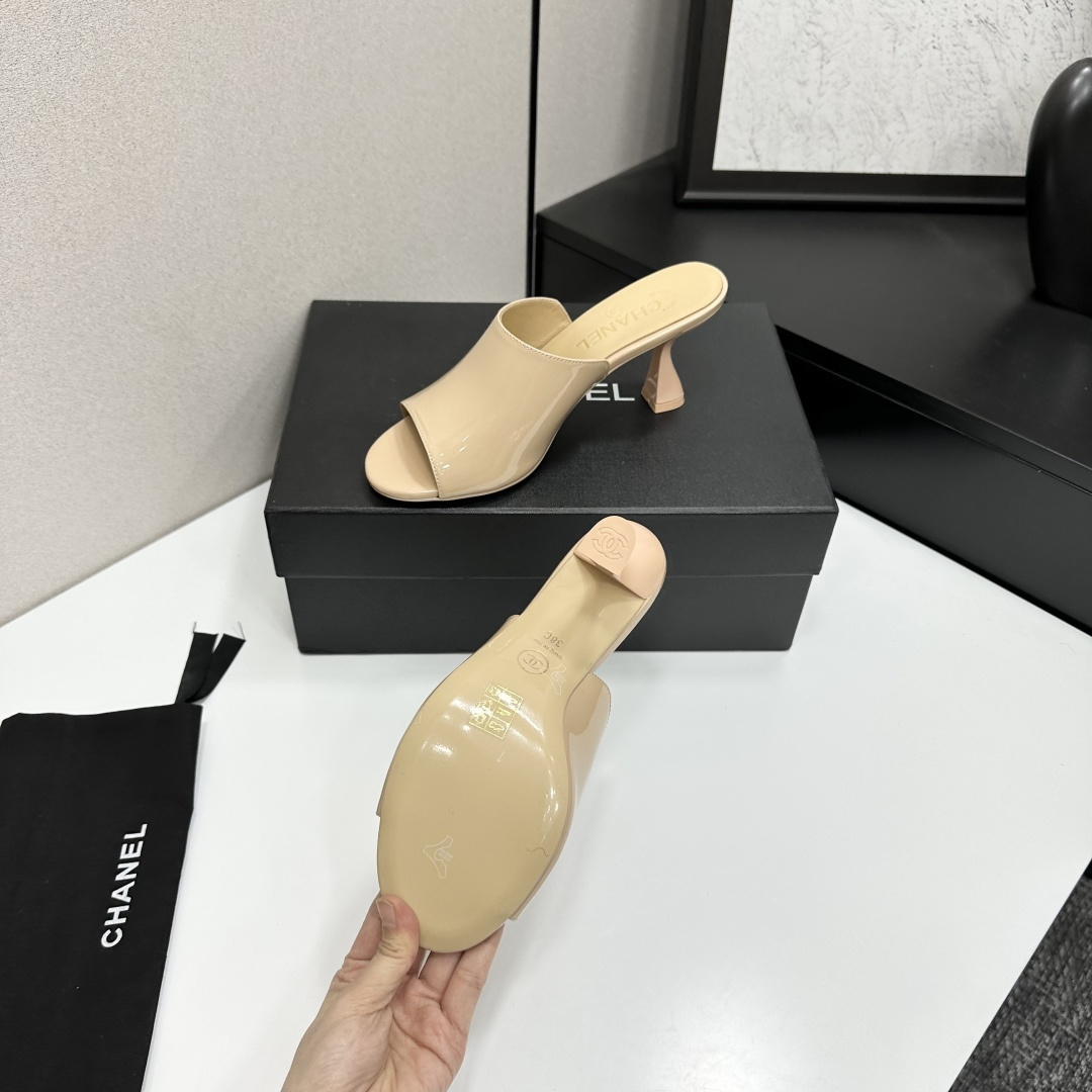 A pair of Chanel beige patent leather open-toe mules with gold CC logo and sculptural hourglass heels displayed on a black Chanel box. - Hình 5