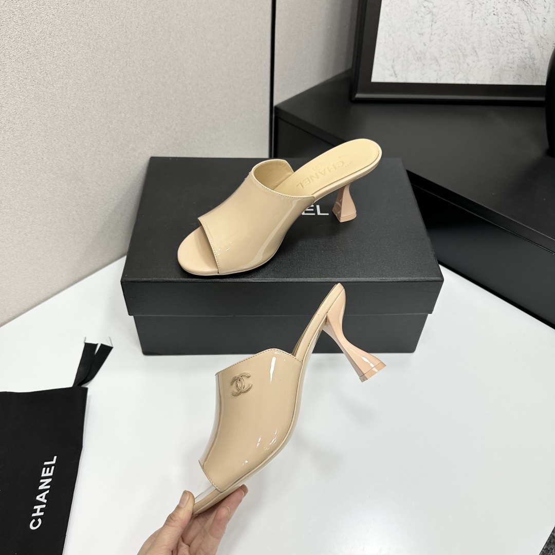 A pair of Chanel beige patent leather open-toe mules with gold CC logo and sculptural hourglass heels displayed on a black Chanel box. - Hình 4