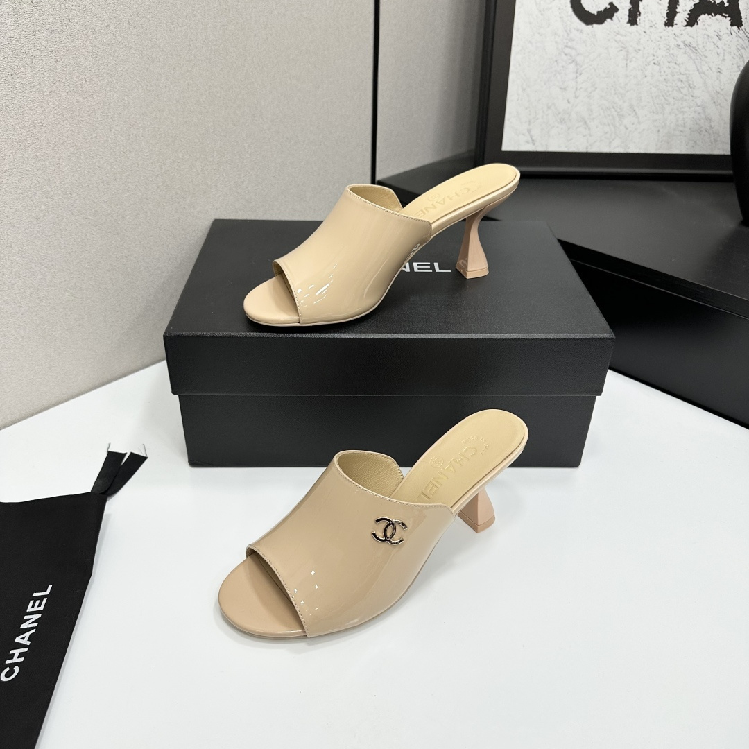 A pair of Chanel beige patent leather open-toe mules with gold CC logo and sculptural hourglass heels displayed on a black Chanel box. - Hình 3