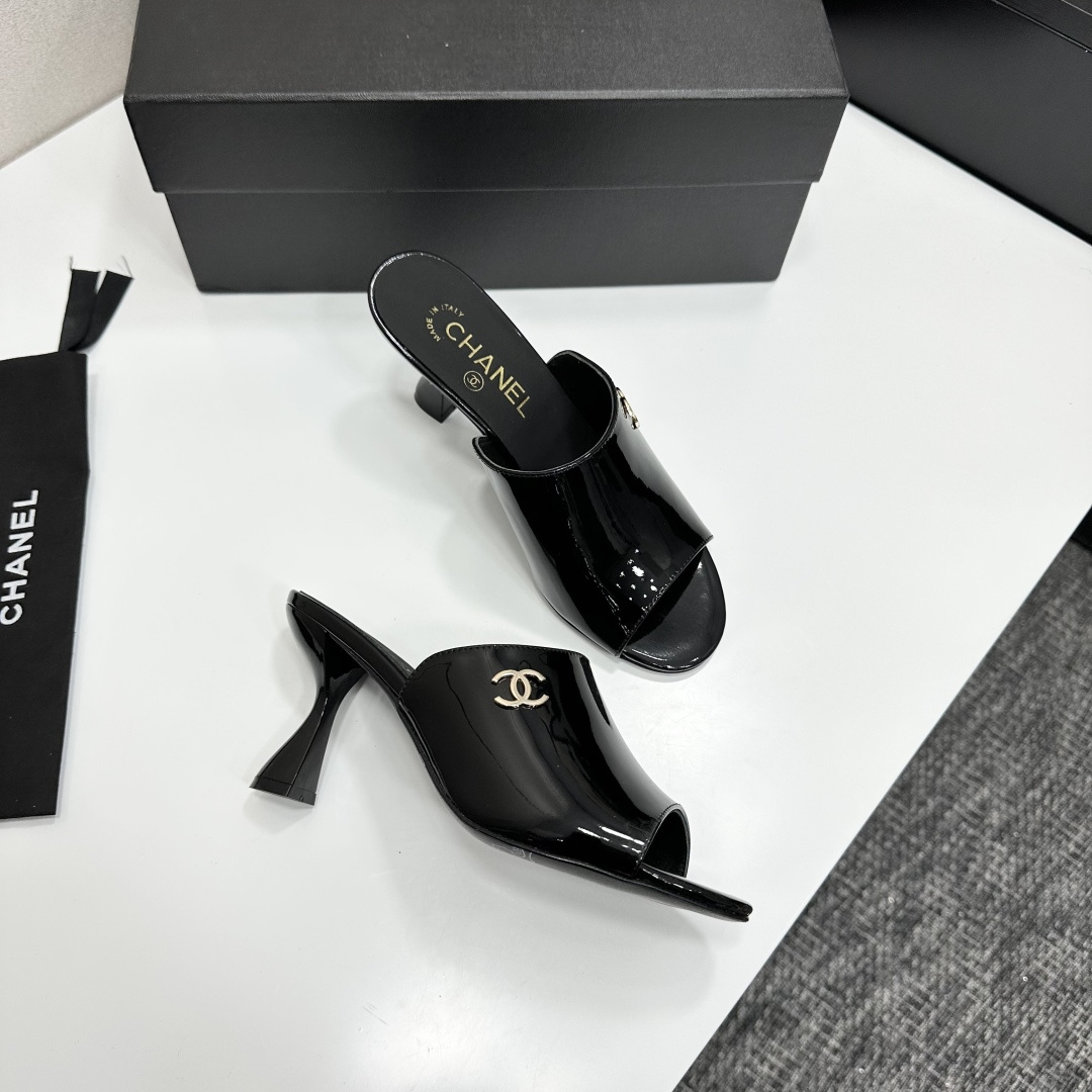 Pair of Chanel black patent leather mules with gold CC logo and sculptural high heels displayed on a black designer box. - Hình 9