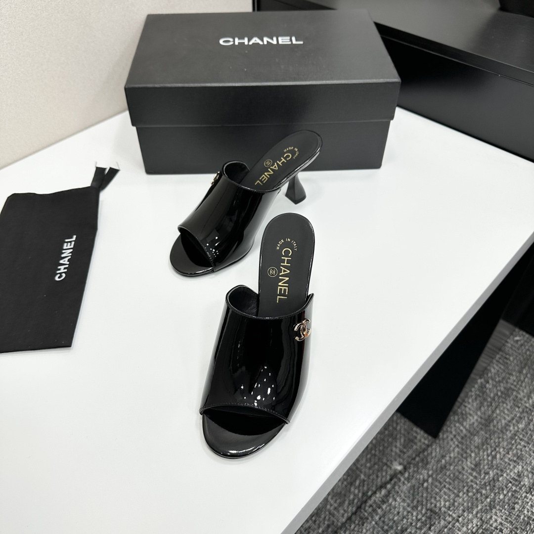 Pair of Chanel black patent leather mules with gold CC logo and sculptural high heels displayed on a black designer box. - Hình 6