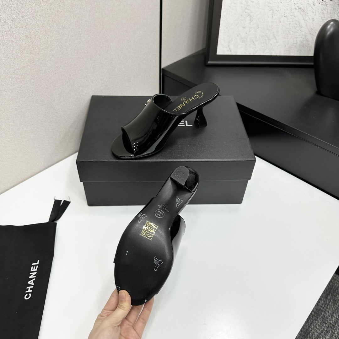 Pair of Chanel black patent leather mules with gold CC logo and sculptural high heels displayed on a black designer box. - Hình 5