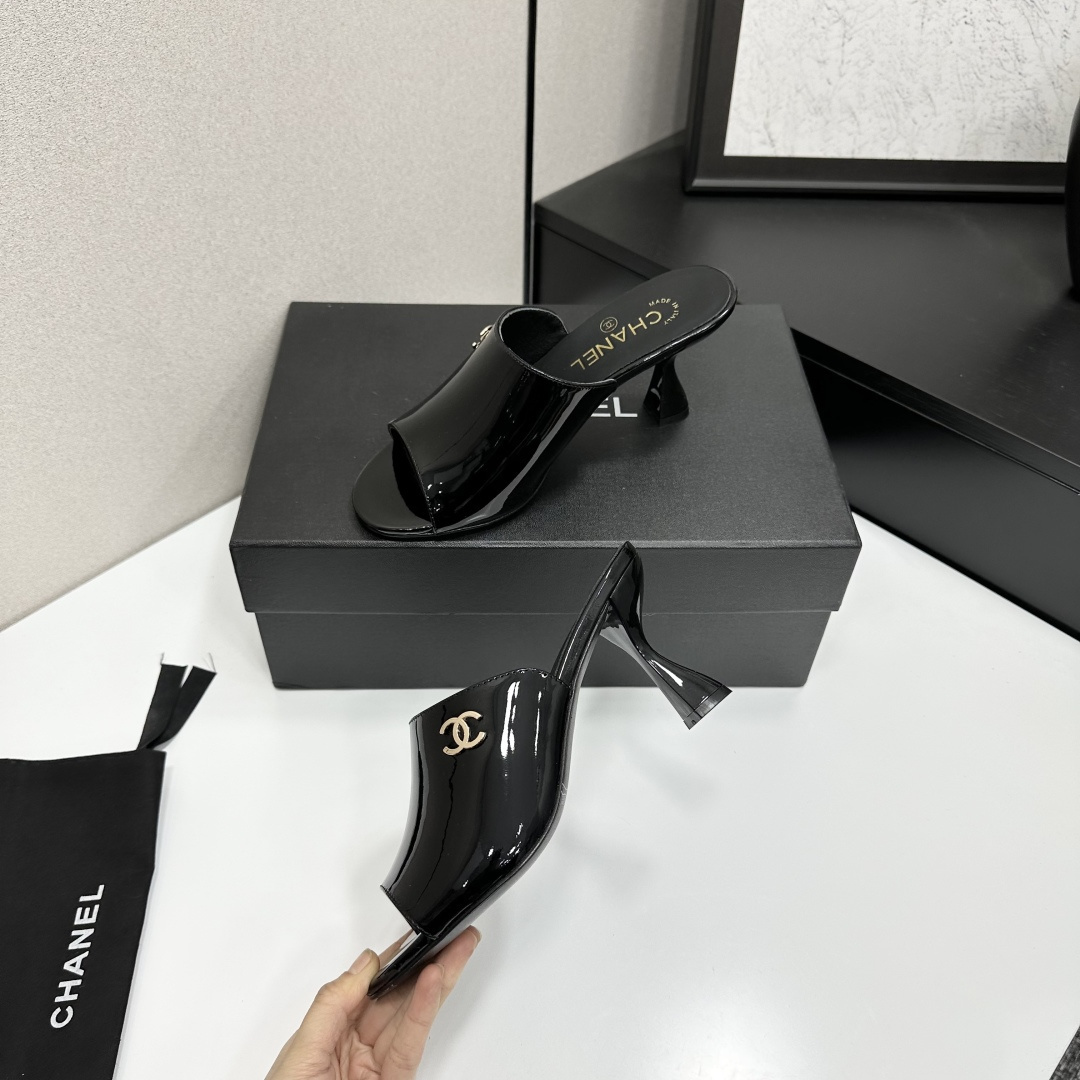 Pair of Chanel black patent leather mules with gold CC logo and sculptural high heels displayed on a black designer box. - Hình 4