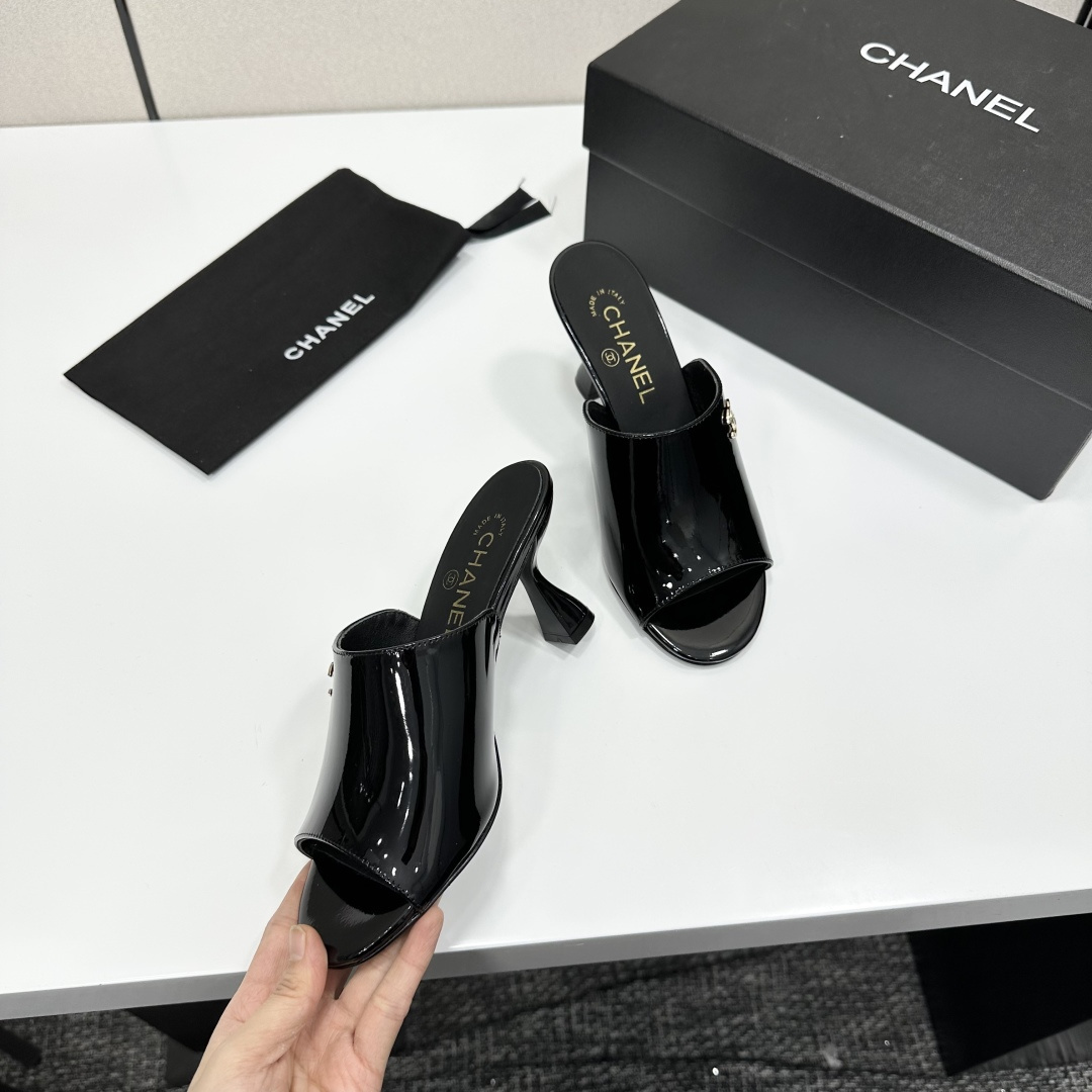 Pair of Chanel black patent leather mules with gold CC logo and sculptural high heels displayed on a black designer box. - Hình 2
