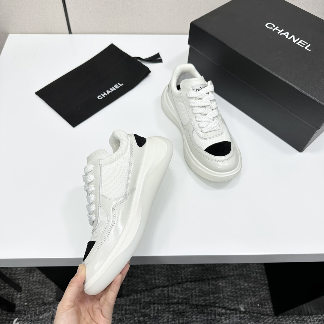 A pair of Chanel white mesh sneakers with black accents and a chunky white sole sitting on a black designer box. - Hình 2