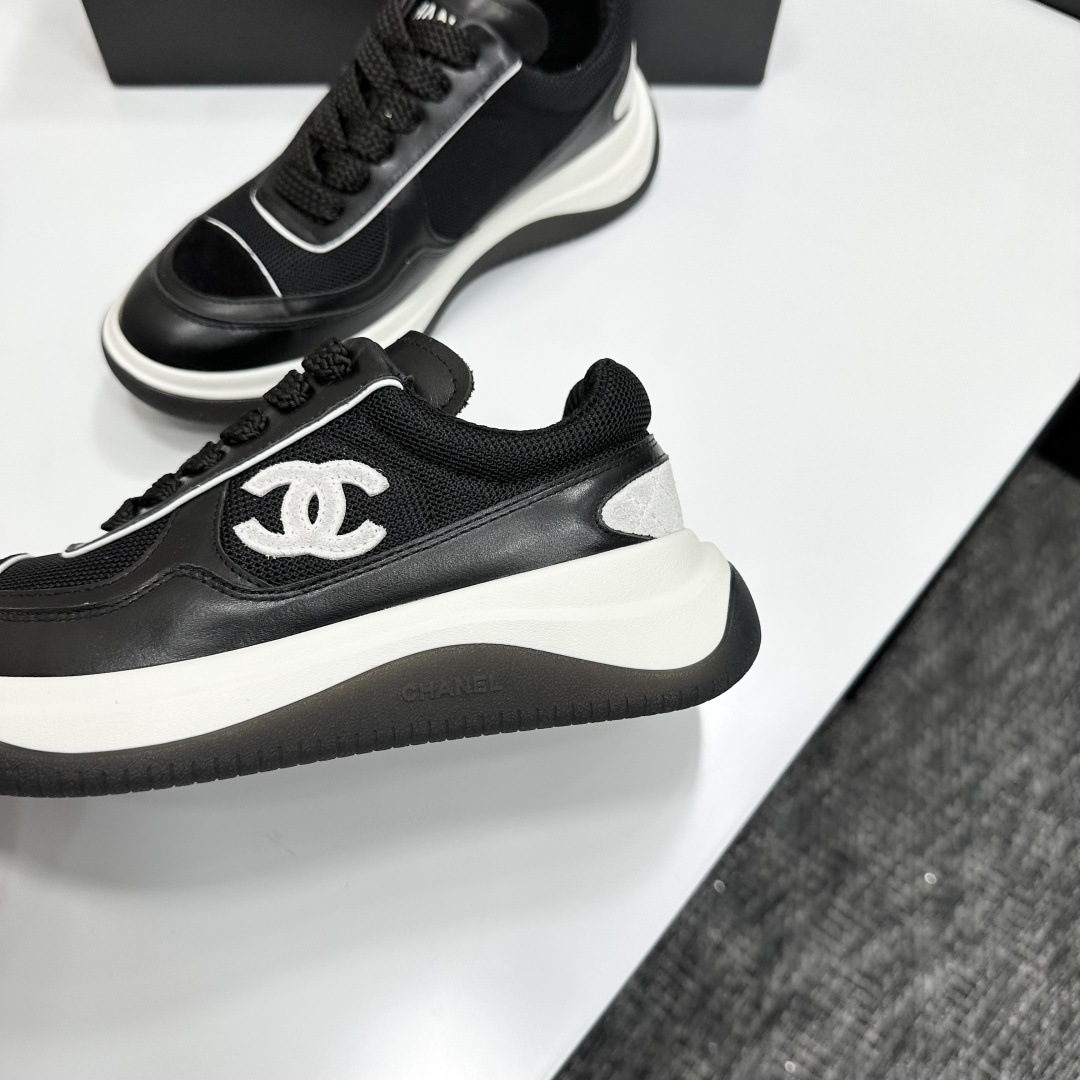 A pair of Chanel black and white mesh leather sneakers with the white interlocking CC logo on the side, placed on a black Chanel shoe box. - Hình 7