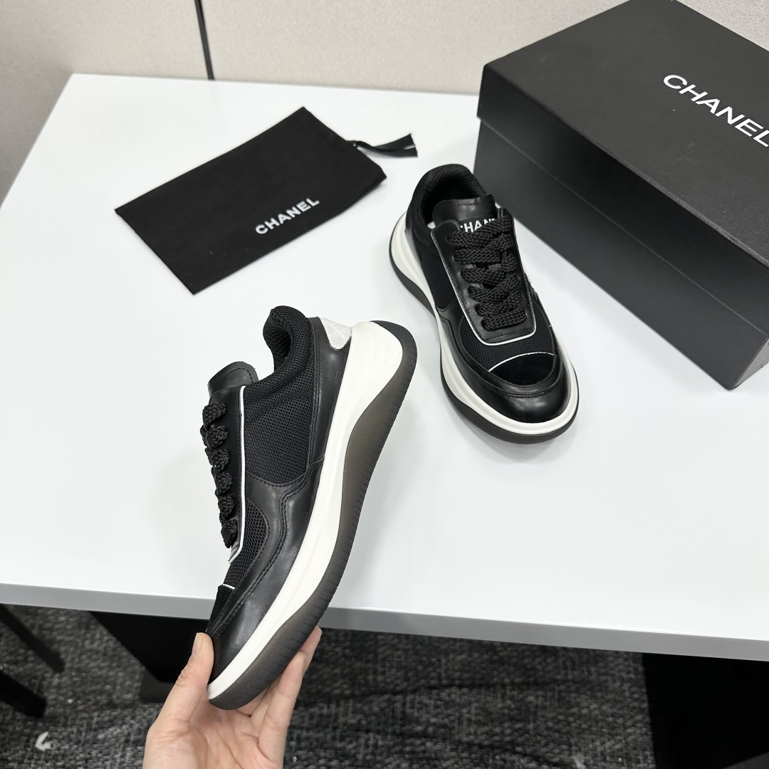 A pair of Chanel black and white mesh leather sneakers with the white interlocking CC logo on the side, placed on a black Chanel shoe box. - Hình 2